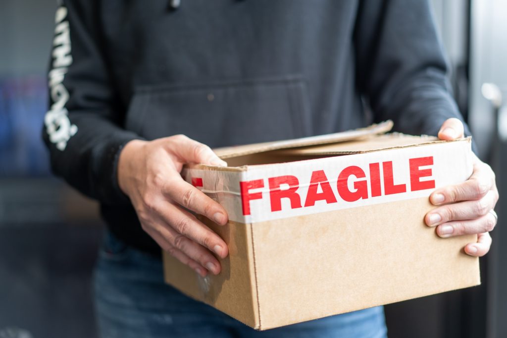 person holding a cardboard box with packaging tape saying fragile