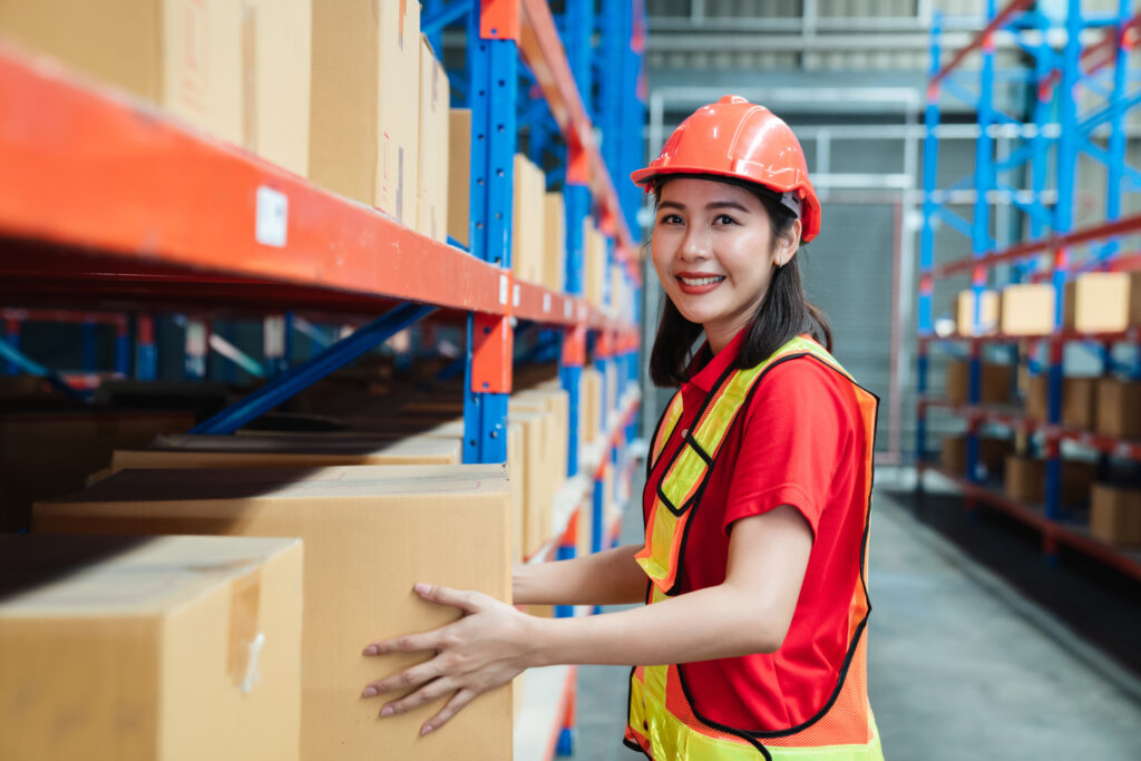 Welpac packaging company Asian warehouse worker proficient in bulk packaging orders, holding boxes in a warehouse.